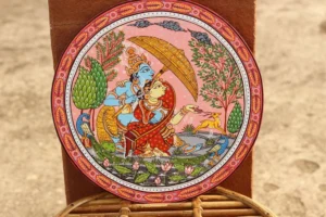 Hand-painted decorative wall plate with two figures under golden canopy, peacock, deer, lotus flowers, and intricate geometric borders in pink, blue, red, and g