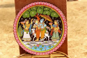 Circular decorative wall plate with traditional painted scene featuring four figures in traditional attire, pink scalloped border, and woven stand