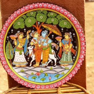 Circular decorative wall plate with traditional painted scene featuring four figures in traditional attire, pink scalloped border, and woven stand