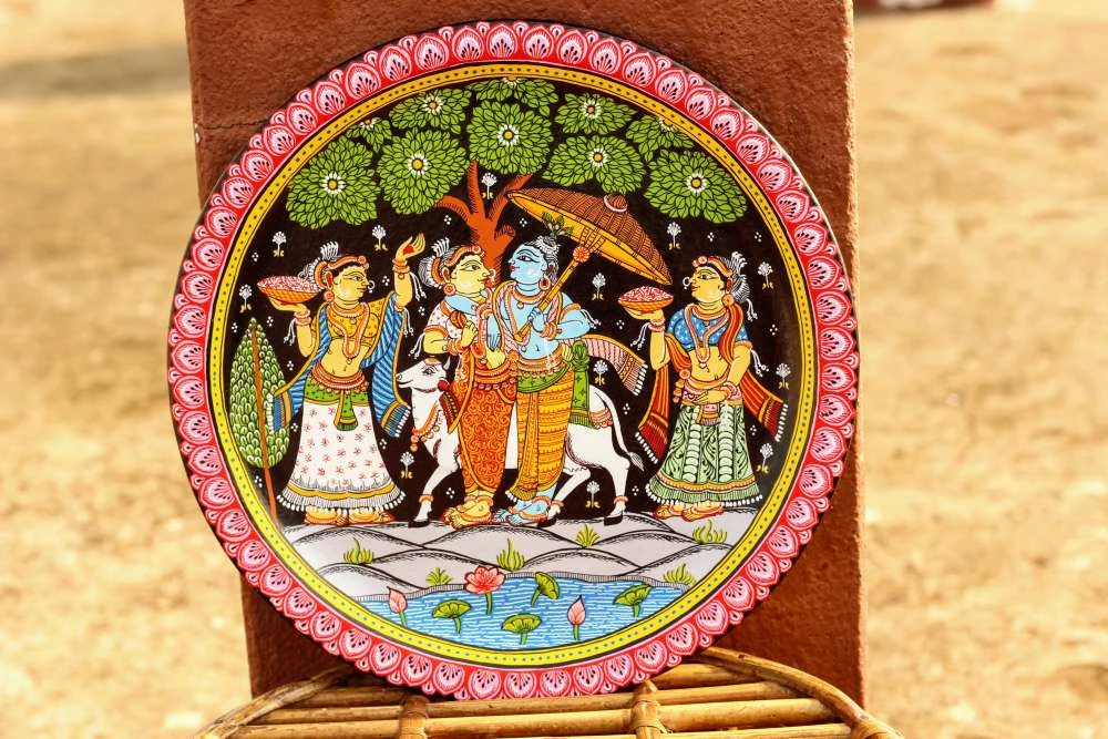 Circular decorative wall plate with traditional painted scene featuring four figures in traditional attire, pink scalloped border, and woven stand